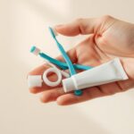 A close-up shot of a human hand holding a set of dental care items, including a toothbrush, dental floss, and a tube of toothpaste, against a clean, minimalist background. The items are arranged neatly, suggesting a sense of organization and attention to detail. The lighting is soft and warm, creating a calming and soothing atmosphere. The overall composition emphasizes the importance of dental hygiene and the steps one can take to promote healthy gums and teeth.